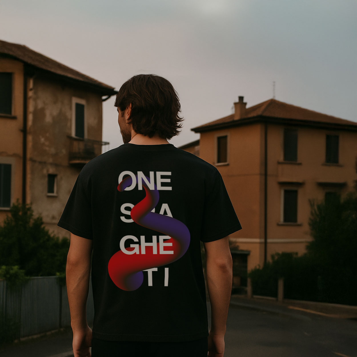 Young man wearing an oversized black One Spaghetti Collezione Unica T-shirt with back print, standing in the Roman suburbs. Limited edition streetwear.